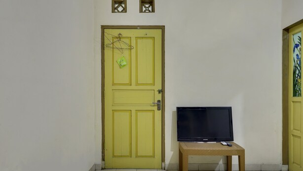 Ein Zimmer mit gelber Tür, einem Fernseher auf einem kleinen Tisch und einem Bett mit weißer Bettdecke.