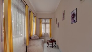 Ein Zimmer mit einer Couch, einem kleinen Tisch und einem fenster mit Vorhängen.