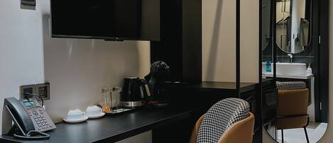A modern hotel room with a black desk, a chair, a coffee maker, and a telephone.