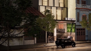 Un hotel moderno con un letrero llamativo, varios pisos y un vehículo estacionado frente a él.