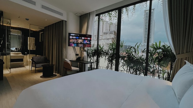 Una habitación de hotel moderna con una cama grande, un escritorio con una silla, un televisor montado en la pared y un balcón con vistas a la ciudad.