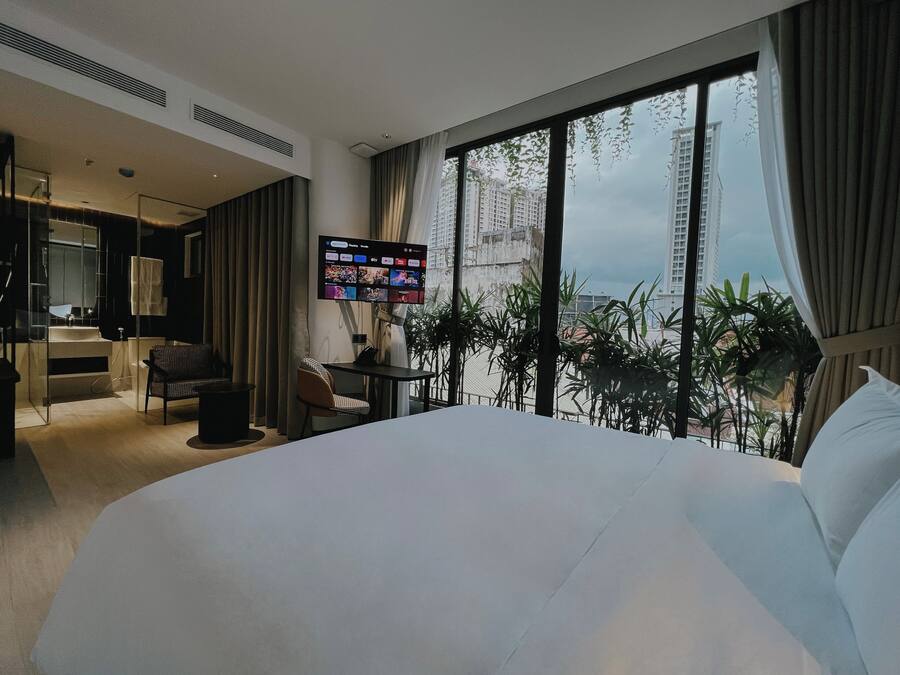 Una habitación de hotel moderna con una cama grande, un escritorio con una silla, un televisor montado en la pared y un balcón con vistas a la ciudad.