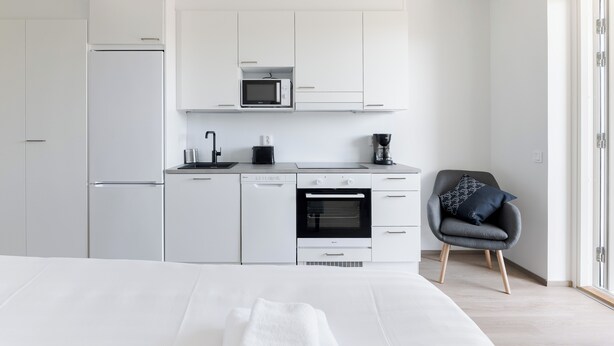 A modern kitchen with white cabinetry, a microwave, a coffee maker, and a built-in oven. - Serviced Apartments Pirkkala by UHANDA  (Pirkkala)