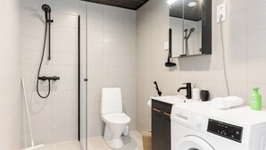 A modern bathroom with a shower, toilet, and washing machine. - Serviced Apartments Pirkkala by UHANDA  (Pirkkala)