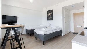 A modern hotel room with two single beds, a desk with a chair, a flat-screen TV, and a painting on the wall. - Serviced Apartments Pirkkala by UHANDA  (Pirkkala)