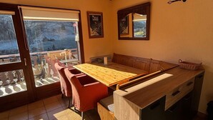 Une pièce chaleureuse avec une table en bois, des bancs et une vue sur un paysage enneigé par une grande fenêtre.