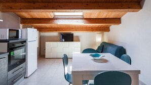 A compact kitchen with a microwave, oven, and white cabinets. There is a dining area with a table and chairs, and a built-in bench with cushions. - Luna d Argento by Wonderful Italy - Kimama (Syracuse)