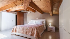 A bedroom with a wooden ceiling, a bed with a patterned bedspread, a bedside table with a lamp, and a wardrobe. - Luna d Argento by Wonderful Italy - Kimama (Syracuse)