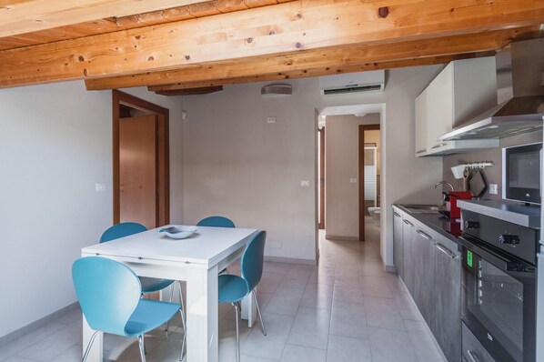 A modern kitchen with stainless steel appliances, a dining area with a white table and blue chairs, and a wooden ceiling.