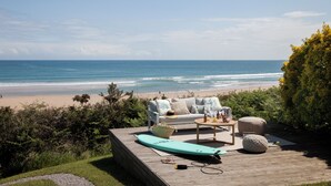 A wooden deck with a sofa, a table, and a surfboard. - Wishome—A Fairytale Home to Extend Summer by the Sea (San Vicente de la Barquera)
