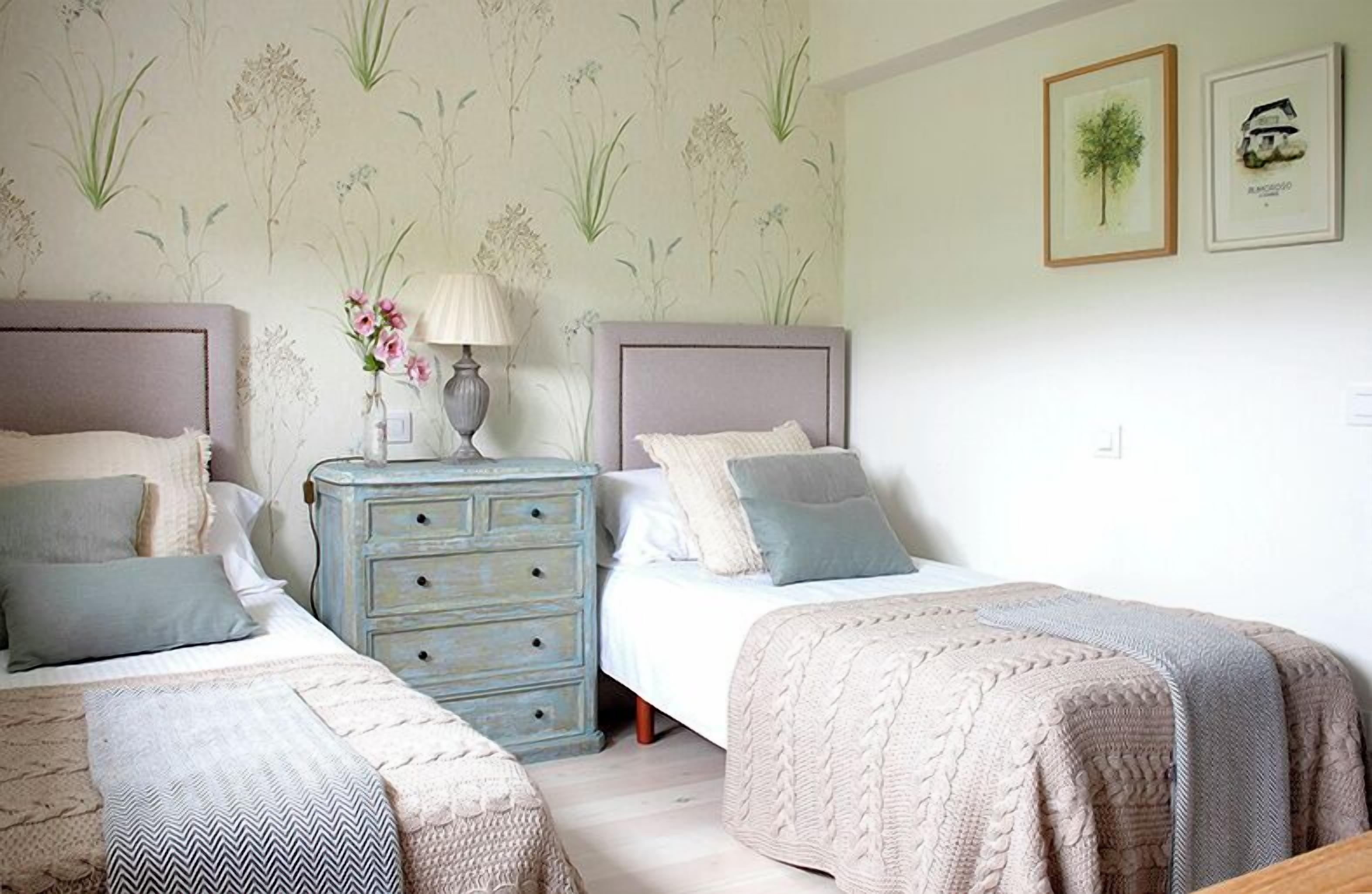 A bedroom with two beds, a dresser, and a wall with floral wallpaper.