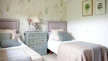 A bedroom with two beds, a dresser, and a wall with floral wallpaper.