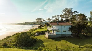 A coastal house with a balcony overlooking the beach, surrounded by lush greenery. - Wishome—A Fairytale Home to Extend Summer by the Sea (San Vicente de la Barquera)