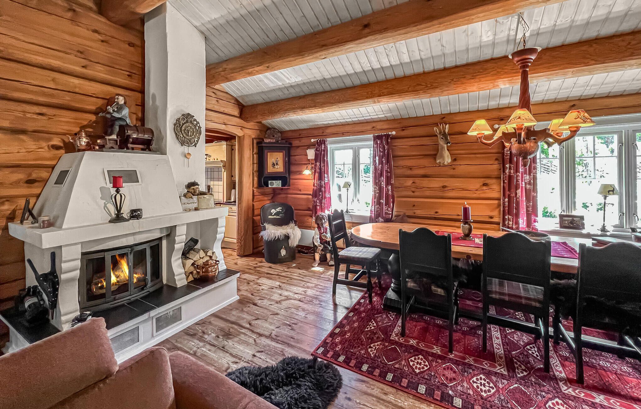 L’intérieur d’un chalet confortable, avec une cheminée, des murs en bois, un coin repas et un lustre.