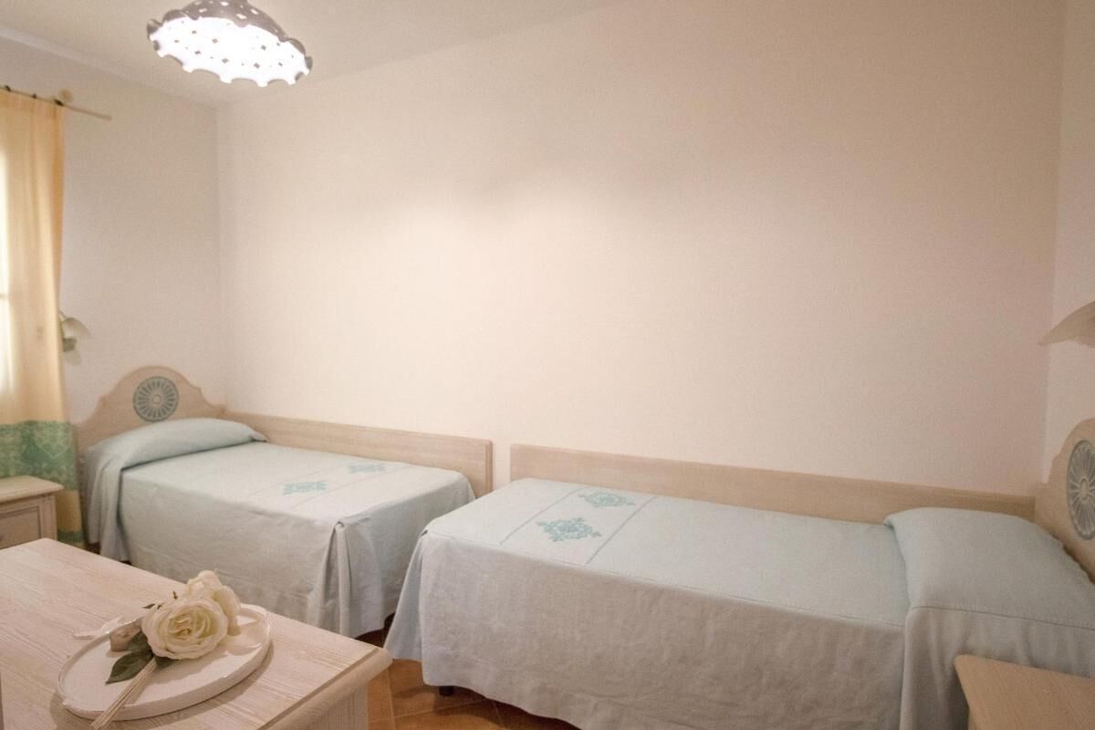 A room with two single beds, a small table with a decorative item, and a simple light fixture.