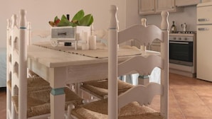 A dining table with a white finish, surrounded by four chairs with woven seat cushions. A small plant and a white container are on the table. - Superb Le Residenze del Golfo di Orosei 1 Bed Room Apartment Sleeps 5 (Orosei)