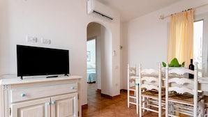 A room with a TV on a cabinet, a dining area with chairs, and a window with curtains. - Superb Le Residenze del Golfo di Orosei 1 Bed Room Apartment Sleeps 5 (Orosei)