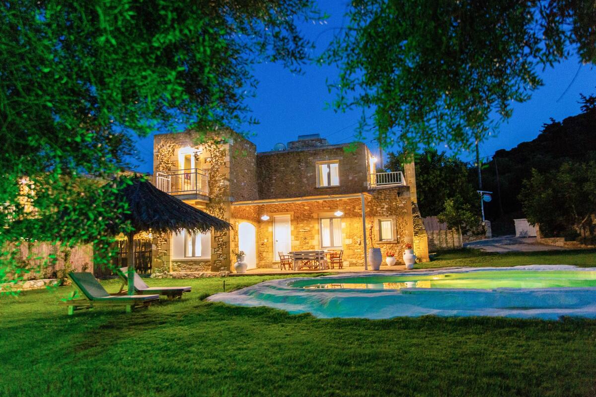 A stone building with a pool, lounge chairs, and a thatched-roof structure.