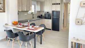 A modern kitchen with light wood cabinets, a black refrigerator, and a dining area with black chairs and a white table. - Phaedra House For Relaxing Holidays Near Platanias (Platanias)