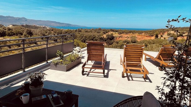 A balcony with wooden chairs, a table with a coffee pot, and a view of the countryside. - Phaedra House For Relaxing Holidays Near Platanias (Platanias)