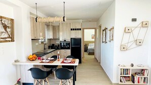 A modern kitchen with a central island, black chairs, and a bookshelf. - Phaedra House For Relaxing Holidays Near Platanias (Platanias)