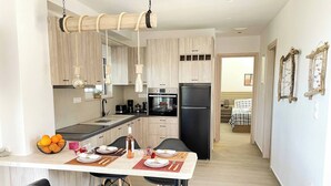 A modern kitchen with wooden cabinets, a black refrigerator, and a dining area with black chairs and a table set for two. - Phaedra House For Relaxing Holidays Near Platanias (Platanias)