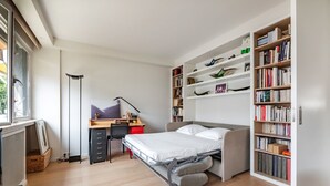 A modern bedroom with a bed, a desk, a chair, a bookshelf, and a radiator. - Contemporary Heights, by Veeve (Paris)