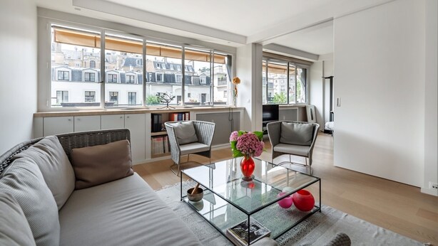 A modern living room with a sofa, two armchairs, a glass coffee table, and a view of the city through large windows. - Contemporary Heights, by Veeve (Paris)