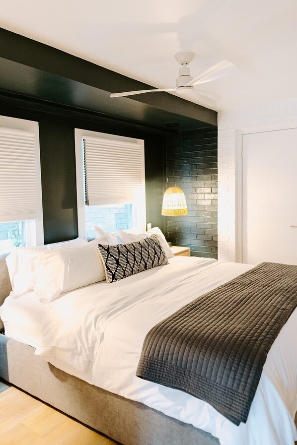 A bedroom with a bed, a nightstand, a ceiling fan, and a window with blinds.
