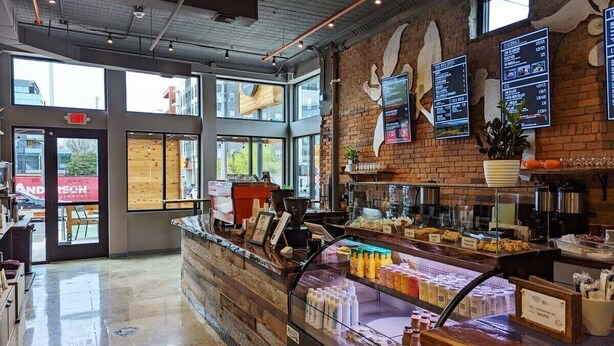 A modern cafe interior with a brick wall, large windows, a counter with beverages, and menu boards. - Musician's Suite: Luxe Music Row Stay, Walk to Gulch! (Nashville)