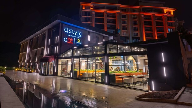 A modern hotel with a glass facade, a pool area, and outdoor seating. - Q Style Hotel  (Trabzon)