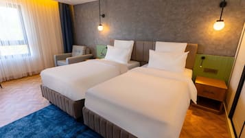 A hotel room with two beds, a sofa, a nightstand, and a window with curtains.