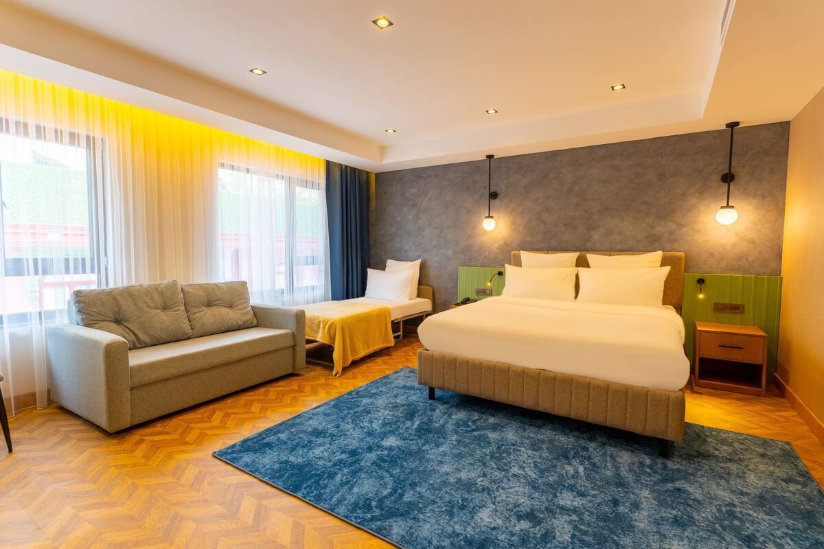 A modern hotel room with a large bed, a sofa, a small table, and a nightstand.