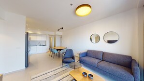A modern living room with a sofa, a coffee table, and a dining area with chairs and a table. - Savyon V.I.E.W - Luxury 3BR w/ Har HaBayit View (Jerusalem)