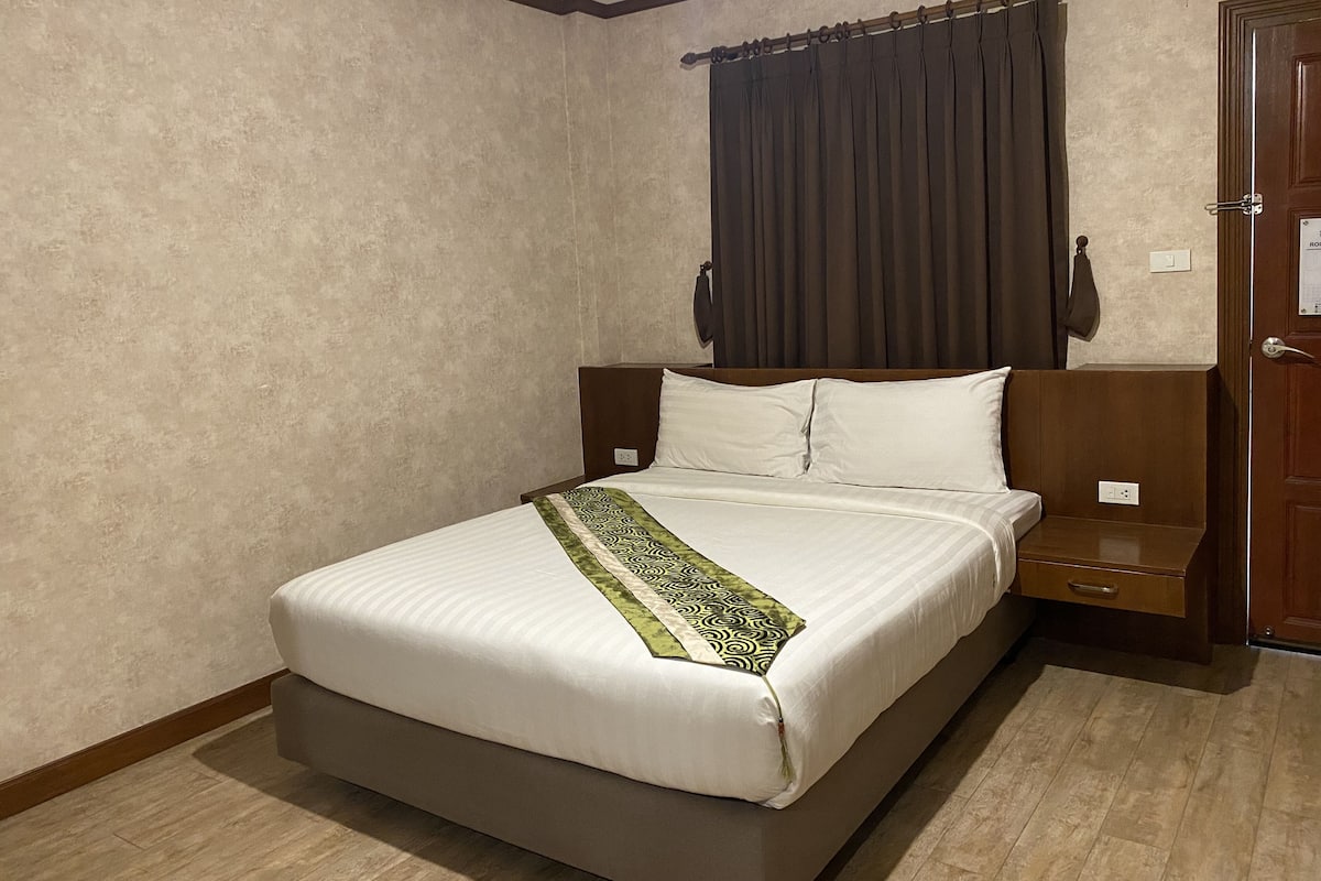 A neatly made bed with a patterned throw, a wooden headboard, and a nightstand with a lamp.
