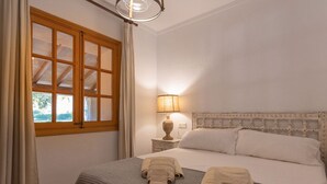 Un dormitorio con cama, una mesita de noche con lámpara y una ventana con cortinas.