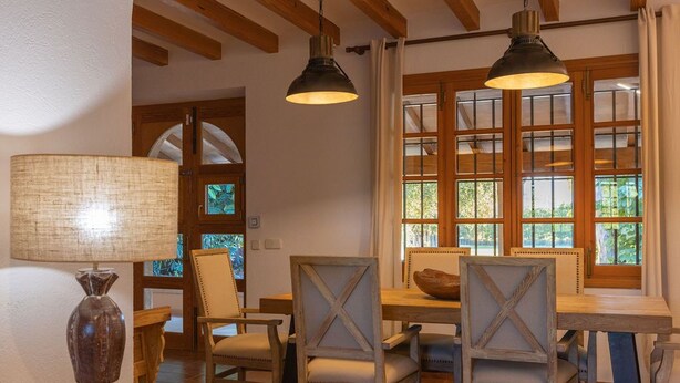 Un comedor con muebles de madera, dos lámparas colgantes y vistas amplias por los ventanales.