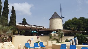 A pool area with blue lounge chairs, a white building with a conical roof, and a sign indicating a no swimming zone.