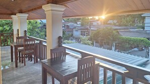 A covered outdoor seating area with wooden tables and chairs, a tiled floor, and a view of a residential neighborhood. - Le KhounSok Boutique Hotel (Luang Prabang)