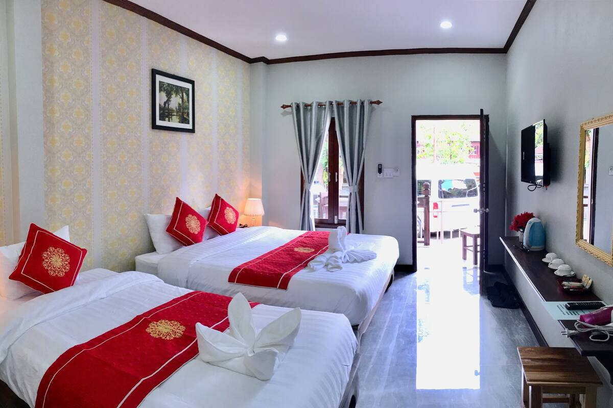 A hotel room with two beds, a desk, a mirror, and a view of the outdoors.