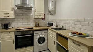 Cocina compacta con armarios blancos, horno empotrado, microondas, lavadora y lavaplatos.