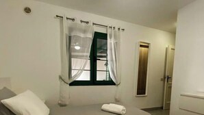 Un dormitorio con cama, almohadas, una ventana con cortinas, un ventilador de techo y una puerta.