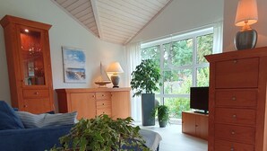 Un salon spacieux avec un haut plafond, un plancher en bois, un canapé bleu, un meuble en bois, un téléviseur et une grande fenêtre donnant sur un paysage verdoyant.