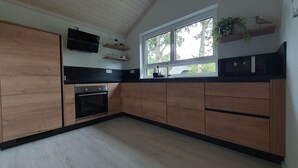 Une cuisine moderne avec des meubles en bois, un four encastré et une fenêtre donnant sur les arbres.