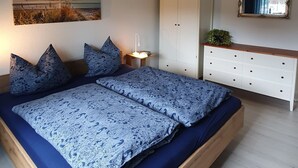 Une chambre avec un plafond en bois, un lit avec une literie bleue, une armoire blanche et un tableau accroché au mur.