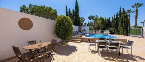 An outdoor patio with a pool, seating arrangements, and a small tree.