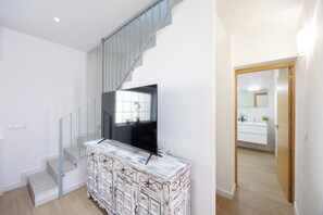 A modern interior with a staircase, a flat-screen TV, and a bathroom visible through an open door.