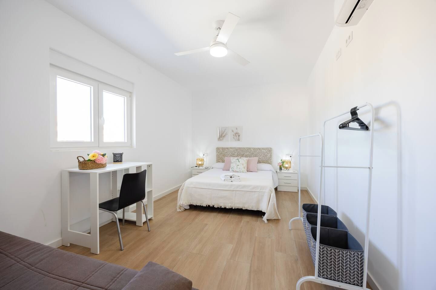 Een slaapkamer met een bed, nachtkastjes, een bureau, een stoel, een kledingkast en een plafondventilator.