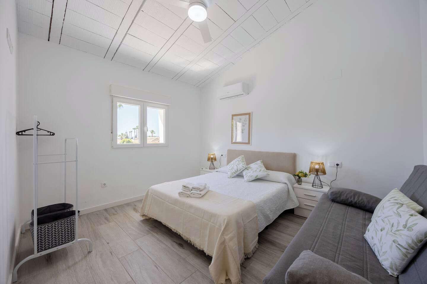 Et soveværelse med seng, sengeborde, et ophængt stativ, et vindue og en ventilator i loftet.