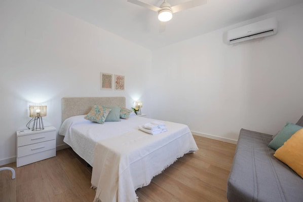 Ein Schlafzimmer mit Bett, Nachttisch, Lampe, Klimaanlage und einer Couch.